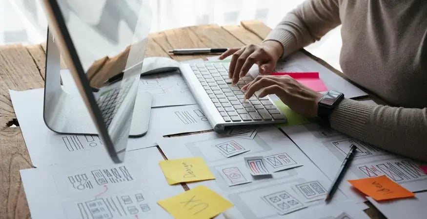 hands typing on a keyboard surrounded by printed paperwork