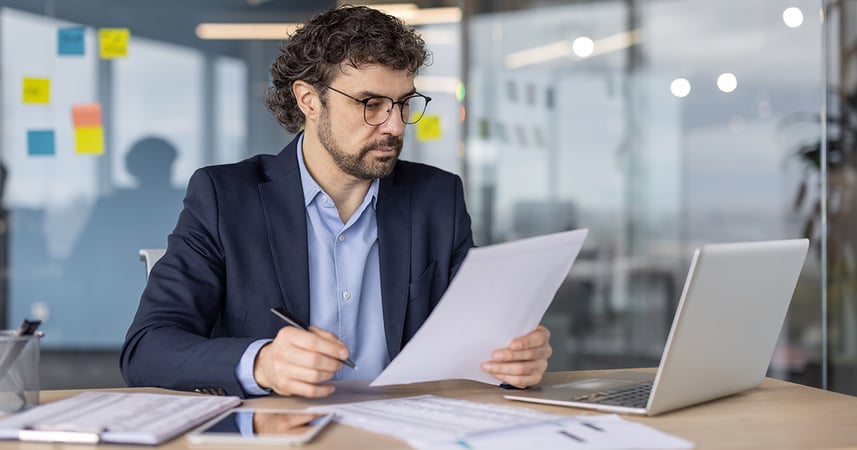 man in office reading printed pages of graphs and charts