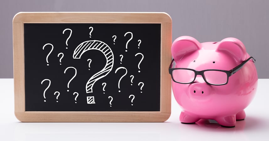Pink piggy bank with eyeglasses next to a small blackboard with question marks drawn on it.