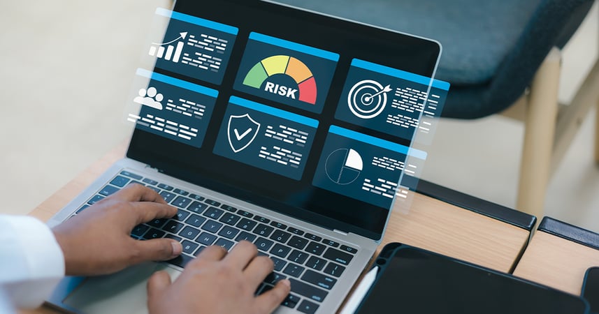 hands on laptop keyboard with graphs and charts on the screen including a multicolored graphic in the center with the word RISK below it