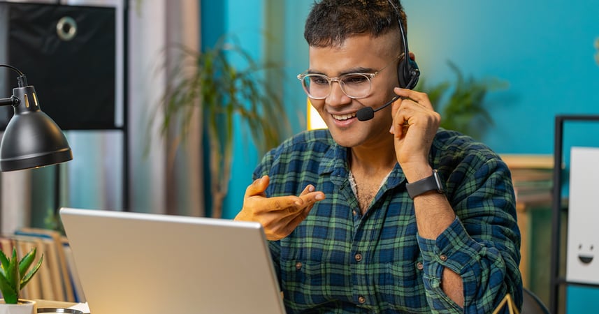 Man working remotely while on a phone call using a headset and laptop computer