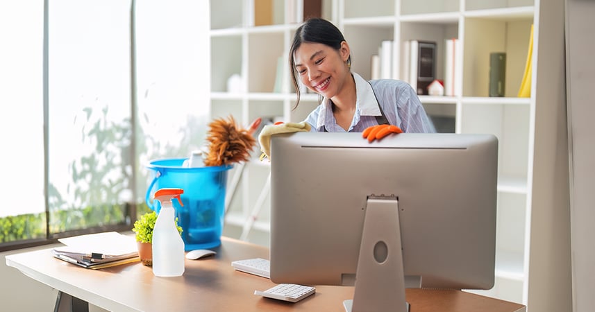 woman cleaning a desk and computer at a workplace