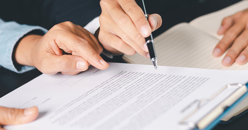 person writing and reviewing a printed contract