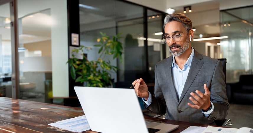 man in office wearing earbud headphones on a call through an app on his laptop computer