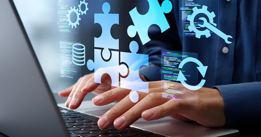 Hands typing on a computer keyboard. Reflection shown of on screen images such as puzzle pieces, gear and wrench and stacks of coins.