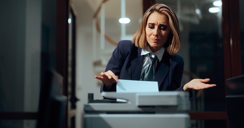Woman looking unhappy pulling a piece of paper off of a shared office printer
