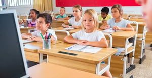 Young students sitting in a classroom with open notebooks.