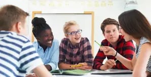 Students sitting at a table in a classroom talking.