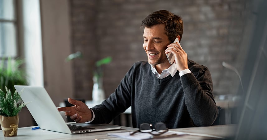 Man speaking on a cell phone while conducting research on his laptop