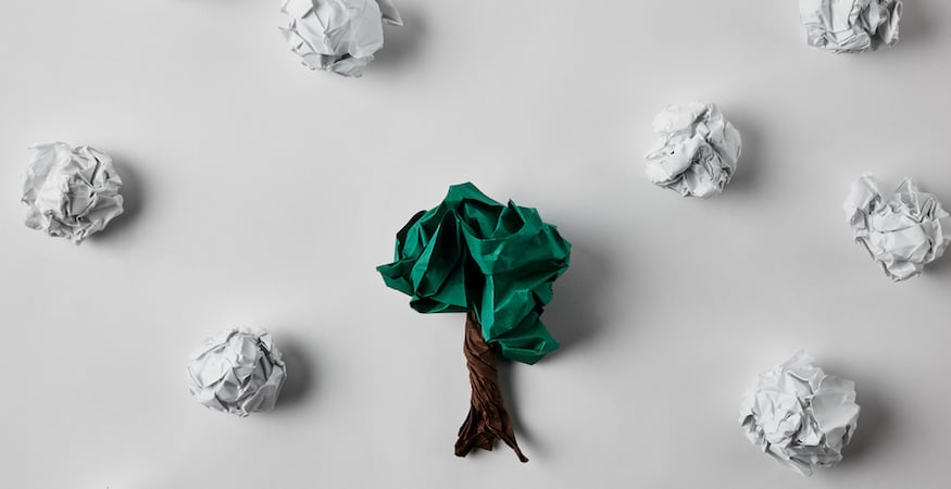 A tree made from brown paper surrounded by crumpled up pieces of white paper