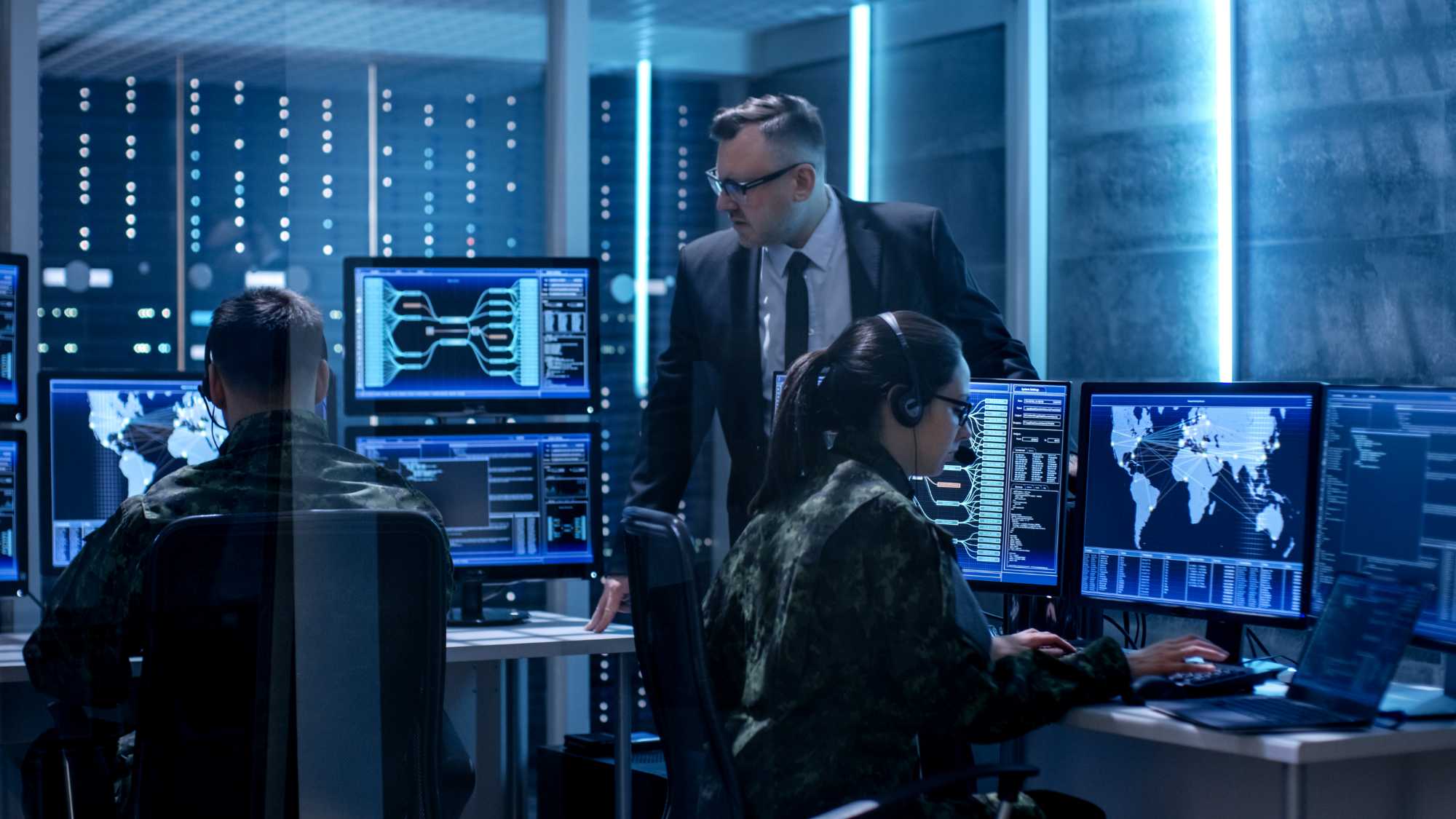 people-in-camo-working-at-computers-with-person-in-suite-watching