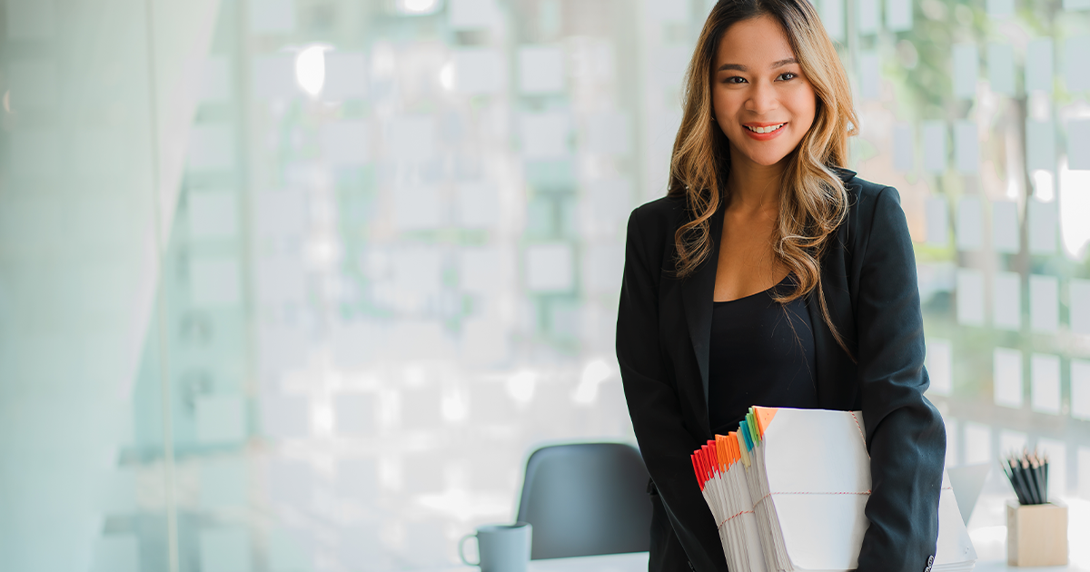 woman in office carrying large stack of printed pages
