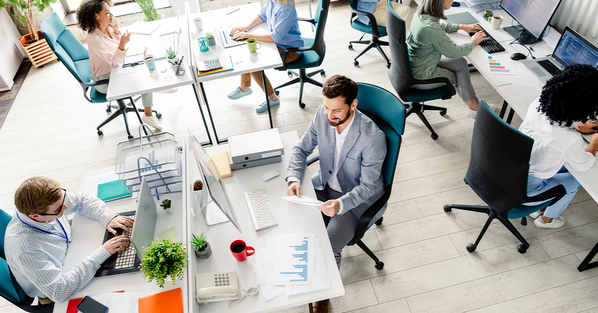busy office with workers at desks with computers and printed papers