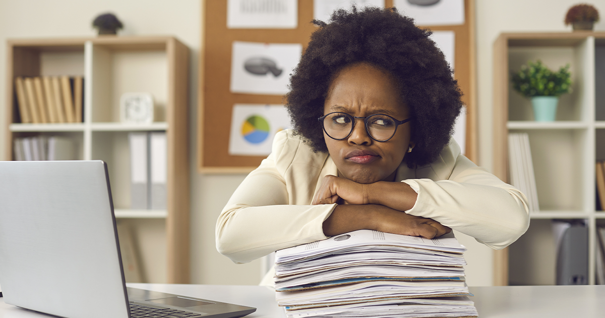 Woman scowling in thought while leaning on a large stack of printed papers