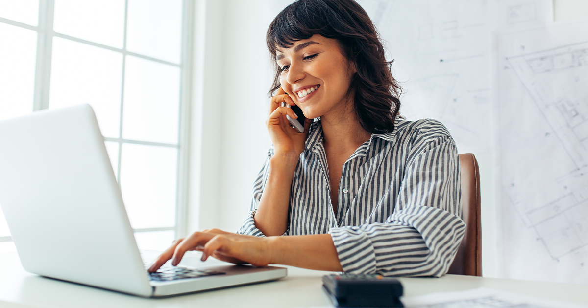 woman talking on mobile phone and typing on laptop