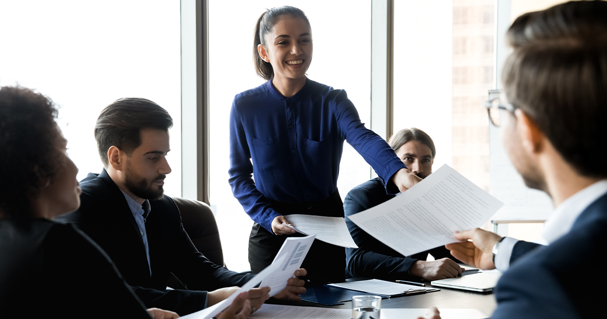 passing out copies of printed pages to meeting attendees seated at a conference room table