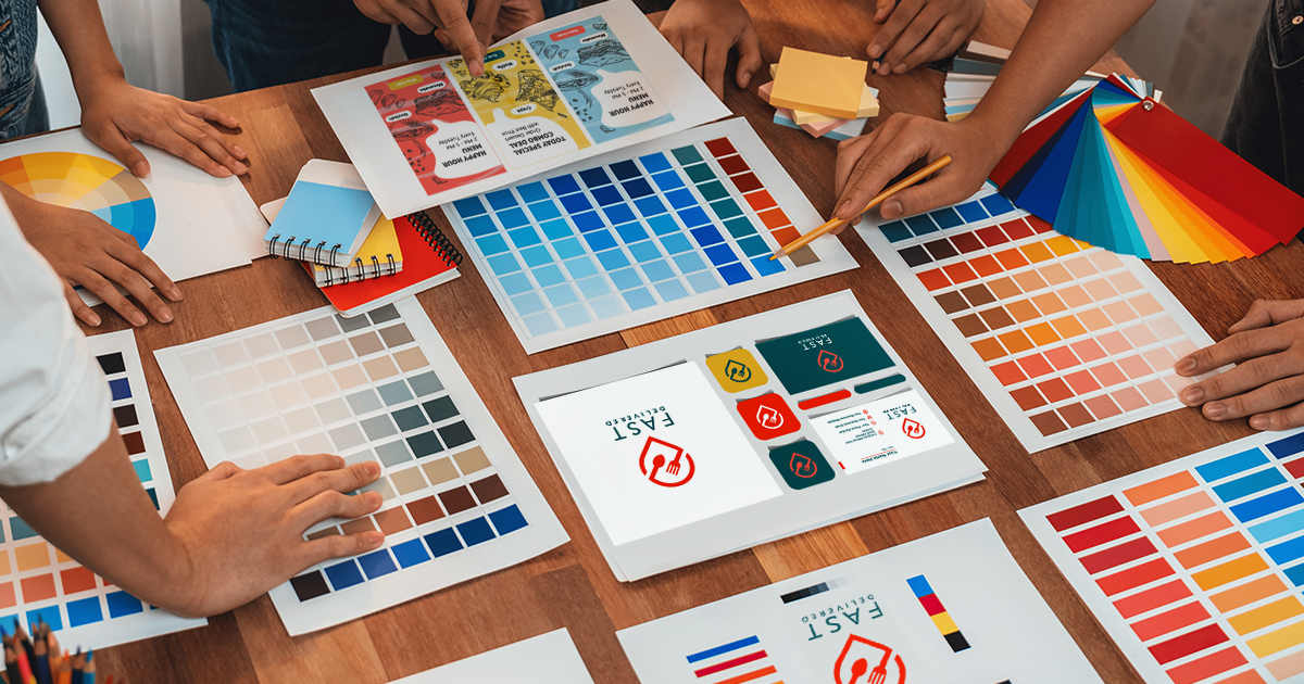 Marketing materials and color charts on a table with the hands of staff pointing out items of interest during a meeting