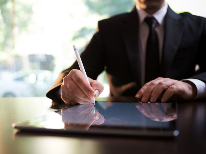 person in suit signing name on tablet