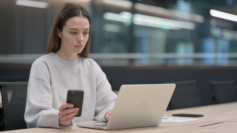 Women holding phone looking at computer screen