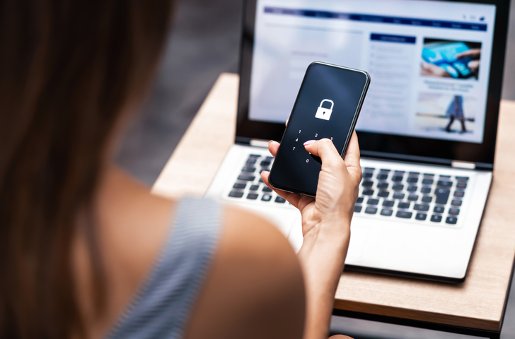 woman looking at smartphone with a lock on it, laptop in background