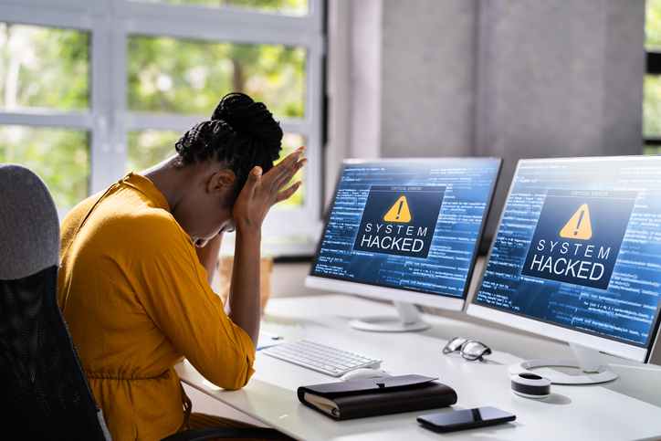 person with head in hands, looking at computer screen that has been hacked
