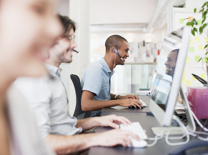 3 people sitting in front of computers with headsets on